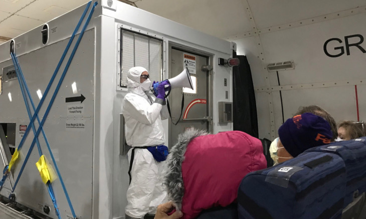 A U.S. health official in a protective suit standing in front of a portable bio-containment unit speaks to U.S. passengers who have chosen to leave the Diamond Princess cruise ship, on a chartered evacuation aircraft in Japan