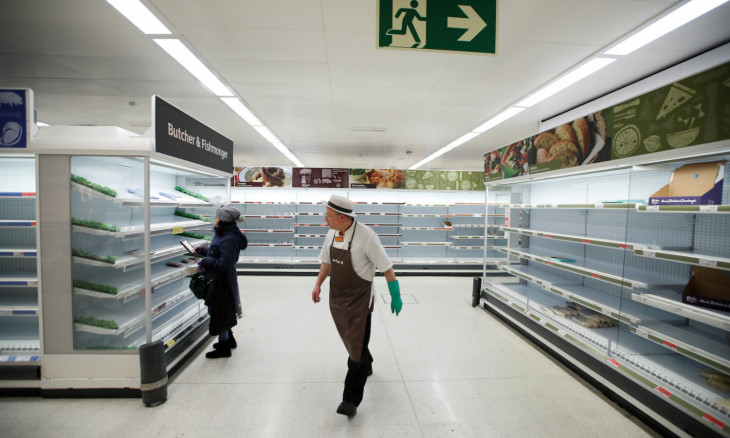 A Sainsbury's worker walks past a customer next to empty shelves at a Sainsbury's store in Harpenden