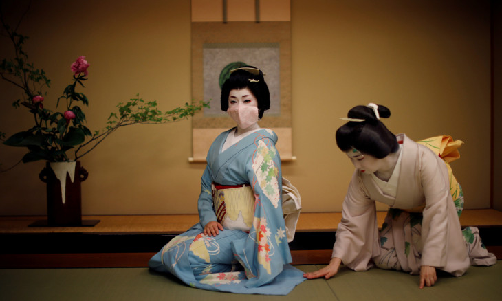 Mayu adjusts Koiku's kimono, both of who are geisha, as Koiku wears a protective face mask 