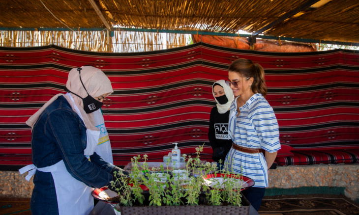 Jordan's Queen Rania watches a woman preparing local produce 