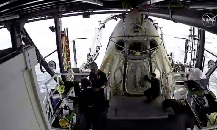 Engineers do a purge of vapor fumes around the Dragon Endeavour with NASA astronauts