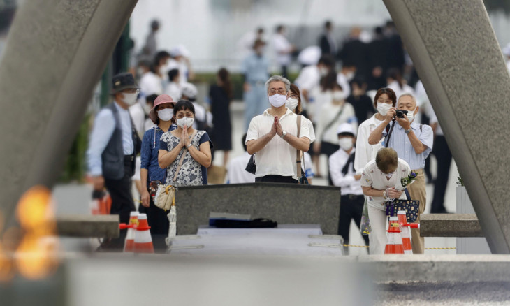 People wearing protective face masks pray for atomic bomb victims in front of the cenotaph for the victims of the U.S.