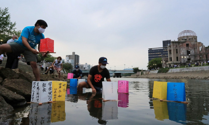 People wearing protective face masks release paper lanterns on the Motoyasu River
