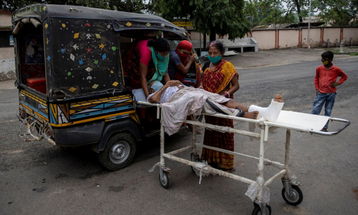 A patient is moved by relatives onto an auto-rickshaw