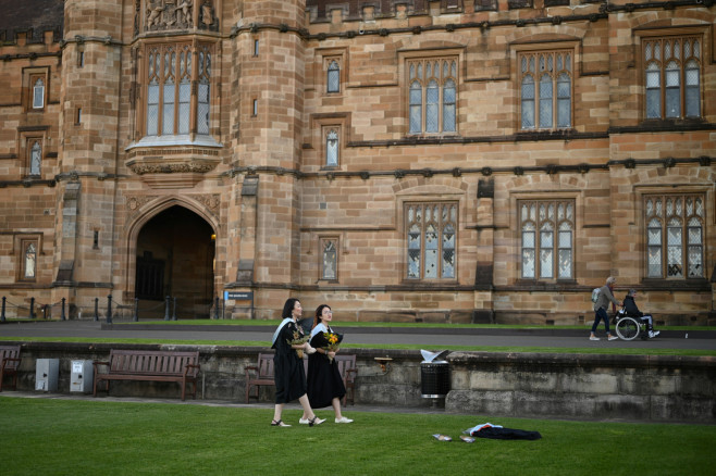 International students Shiyu Bao and Katerina Ma wear graduation gowns as they take pictures around the University of Sydney's campus