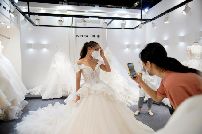 A model wearing a wedding dress poses for a photo as a woman takes a picture of her