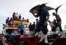Fishermen and their families watch as a worker carries a yellow fin tuna off a fishing boat at fish at a port in General Santos City, Mindanao, southern Philippines January 10, 2008. 