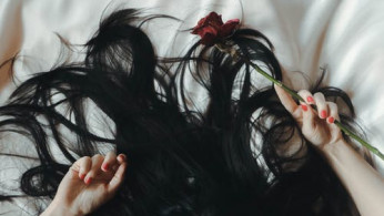 Woman lying on bed with rose on her hand.