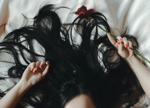 Woman lying on bed with rose on her hand.