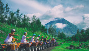 Line of men riding on an ATV with Mayon Volcano as background.
