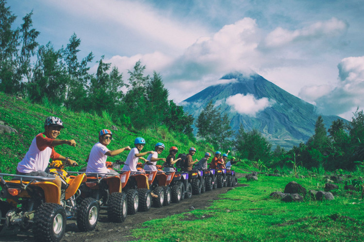 Line of men riding on an ATV with Mayon Volcano as background.