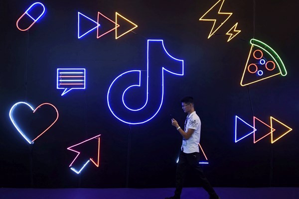 A man holding a phone walks past a sign of Chinese company ByteDance's app TikTok