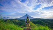 Man wearing white shirt standing in front of Mayon Volcano. 
