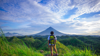 Man wearing white shirt standing in front of Mayon Volcano. 