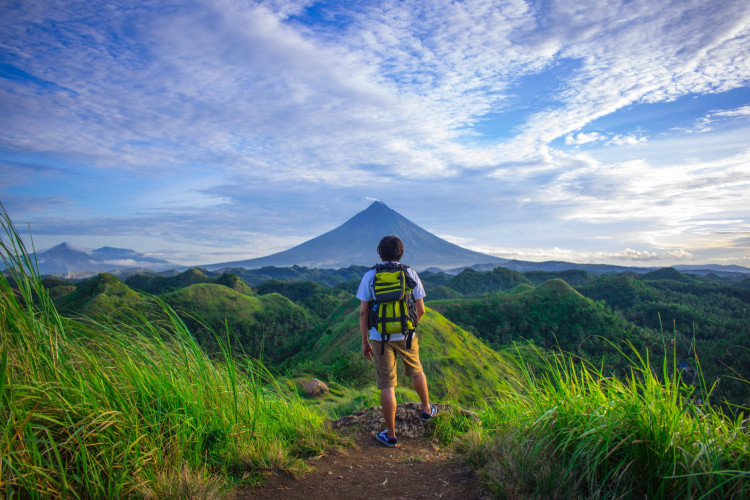 Man wearing white shirt standing in front of Mayon Volcano. 