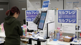 A shopper checks out at an unmanned cash register with using her mobile phone at convenience chain store Lawson in Tokyo