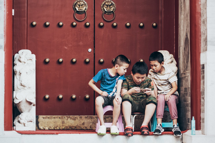Three boys sitting beside the door playing on their mobile phones.