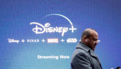 A man looks at his phone as he passes by a screen advertising Walt Disney's streaming service Disney+ in New York