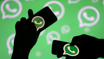 Men pose with smartphones in front of displayed Whatsapp logo in this illustration