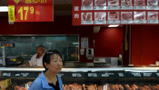 A woman walks past a pork counter at a Walmart in Beijing