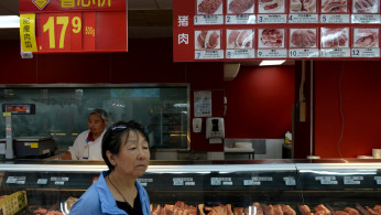 A woman walks past a pork counter at a Walmart in Beijing