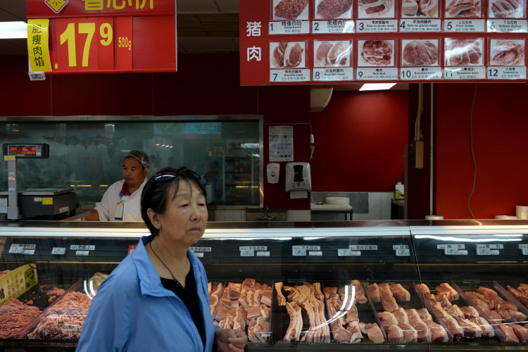 A woman walks past a pork counter at a Walmart in Beijing