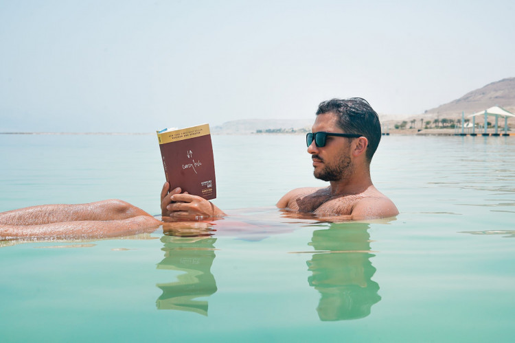 Man wearing book floating while on Dead Sea.