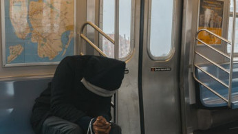 Person in black hoody sitting on train bench.
