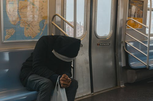 Person in black hoody sitting on train bench.