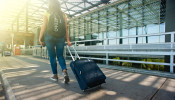 Woman walking on a pathway while strolling luggage.