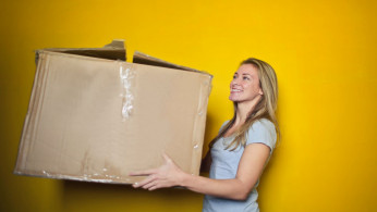 Woman in grey shirt holding a big brown box. 