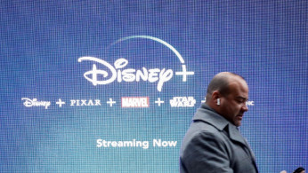 A man looks at his phone as he passes by a screen advertising Walt Disney's streaming service Disney+ in New York