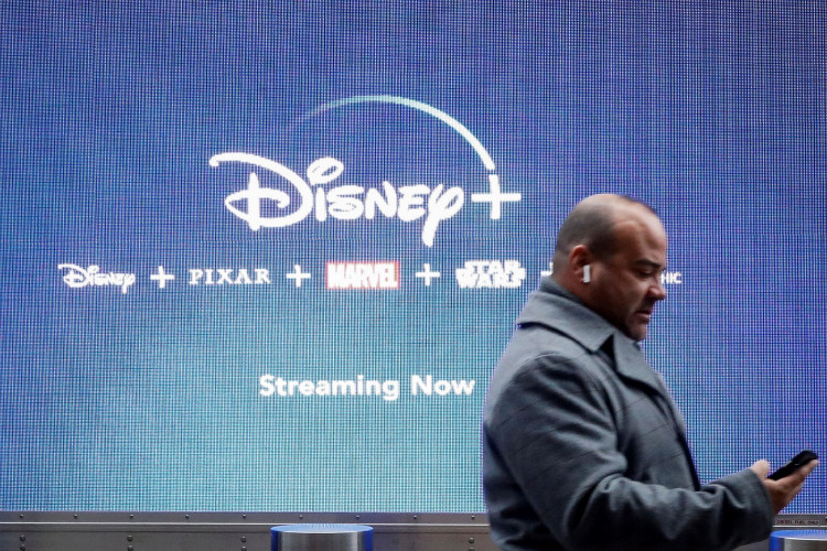 A man looks at his phone as he passes by a screen advertising Walt Disney's streaming service Disney+ in New York