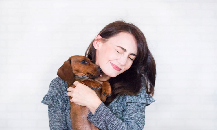 Woman in gray top hugging brown duchshund.