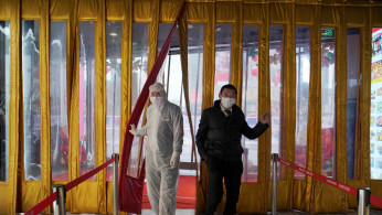 A worker in protective suit walks next to a management staff at an entrance of a shopping mall, as the country is hit by an outbreak of the novel coronavirus, in Beijing