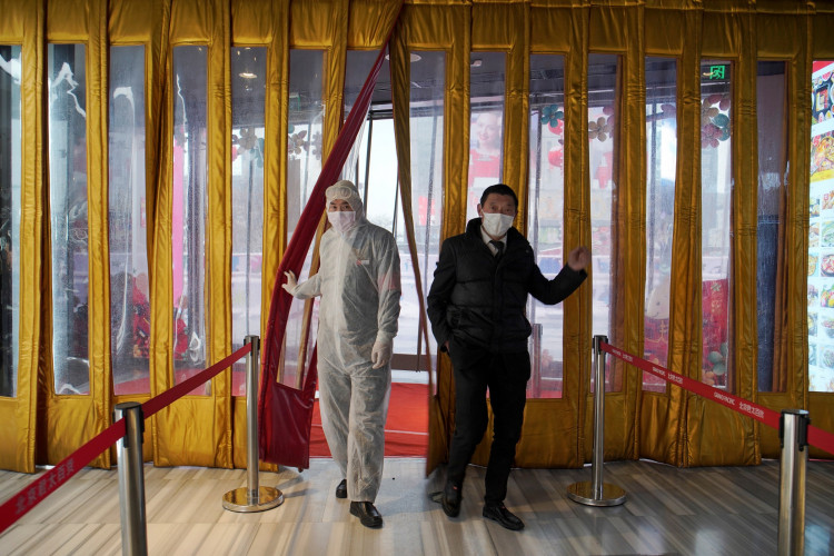 A worker in protective suit walks next to a management staff at an entrance of a shopping mall, as the country is hit by an outbreak of the novel coronavirus, in Beijing
