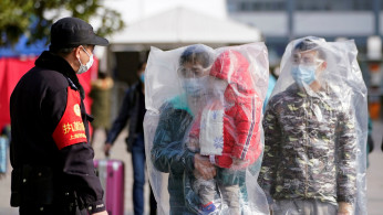 Passengers wearing masks and covered with plastic bags walk outside the Shanghai railway station in Shanghai