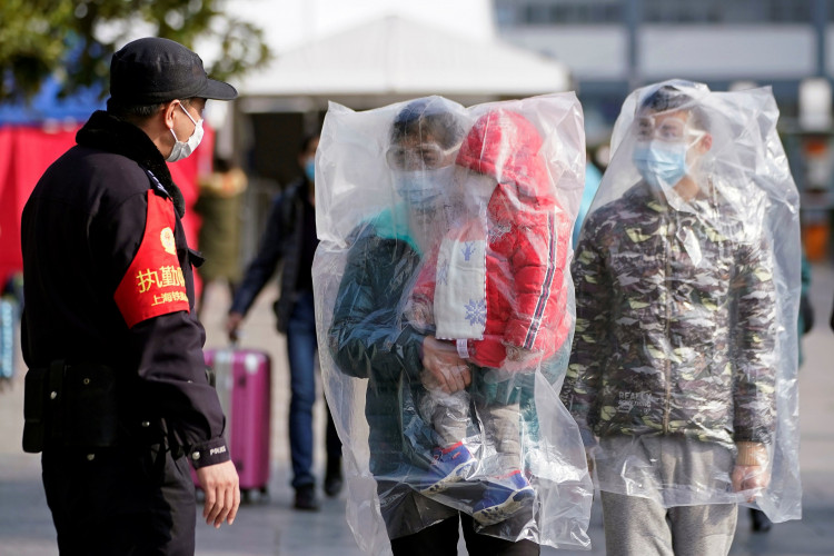 Passengers wearing masks and covered with plastic bags walk outside the Shanghai railway station in Shanghai