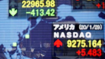 Pedestrians wearing facial masks look at an electric board showing stock averages of Japan's Nikkei and the U.S. Nasdaq outside a brokerage at a business district in Tokyo