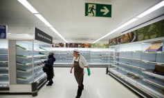 A Sainsbury's worker walks past a customer next to empty shelves at a Sainsbury's store in Harpenden