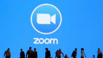 Small toy figures are seen in front of displayed Zoom logo