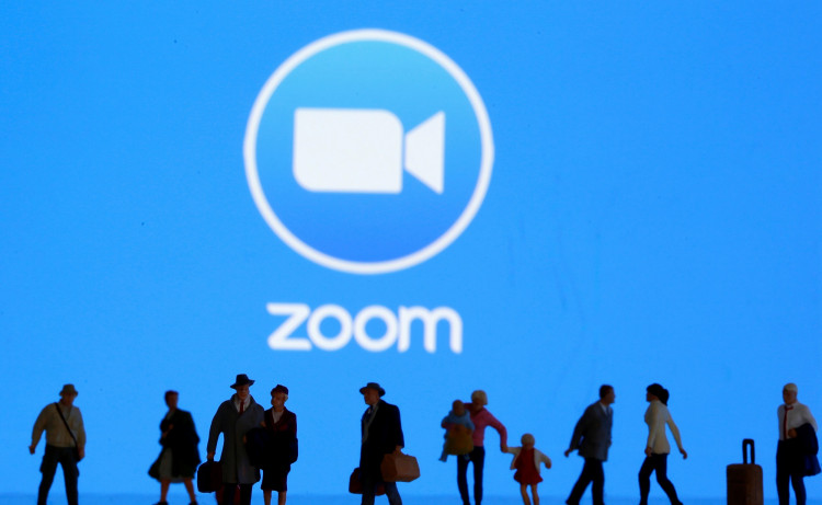 Small toy figures are seen in front of displayed Zoom logo