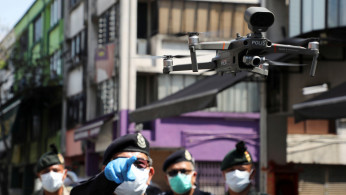 A police officer points at a drone, which is used by Malaysian police to remind citizens to stay at home