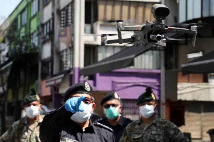 A police officer points at a drone, which is used by Malaysian police to remind citizens to stay at home