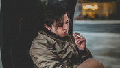 Man wearing gray jacket holding cigarette. 