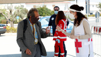 A Red Cross volunteer checks temperature of a customer at the entrance of an open-air food market that has been reopened, during the coronavirus disease (COVID-19) outbreak in Cisternino
