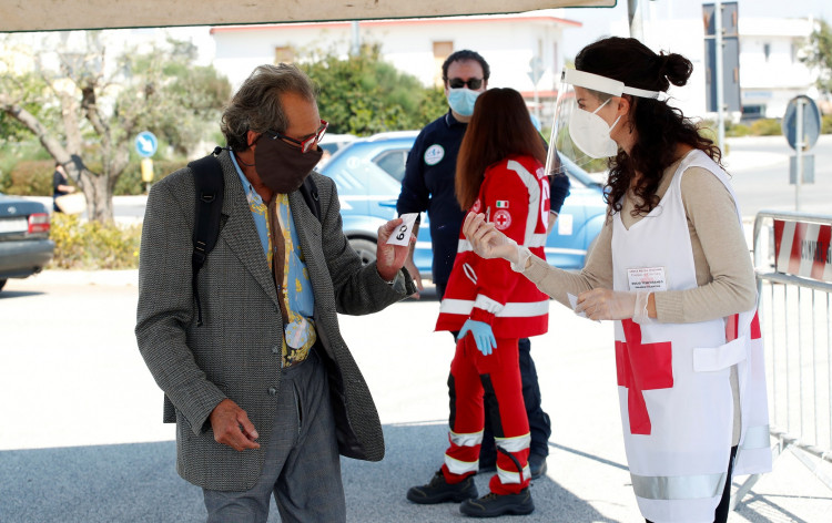 A Red Cross volunteer checks temperature of a customer at the entrance of an open-air food market that has been reopened, during the coronavirus disease (COVID-19) outbreak in Cisternino