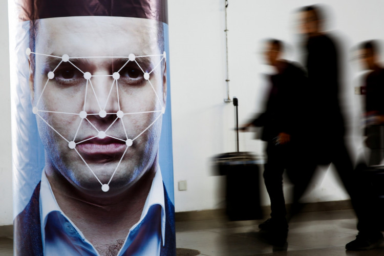 People walk past a poster simulating facial recognition software at the Security China 2018 exhibition