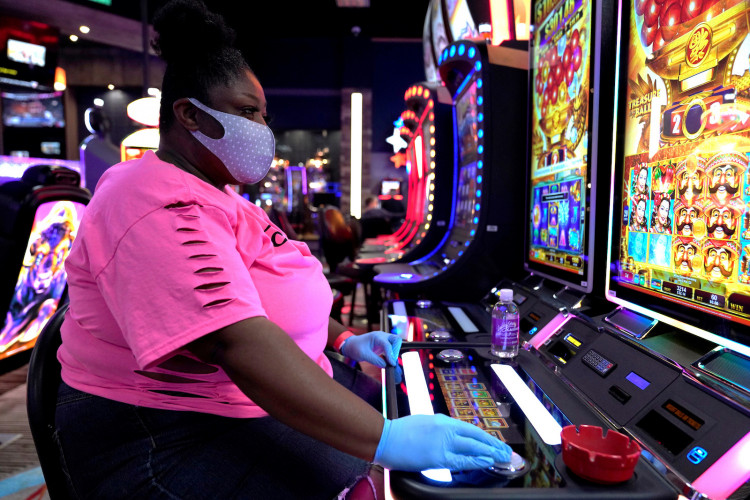A woman wearing a mask and gloves plays a slot machine at the recently reopened Lucky Star Casino in El Reno