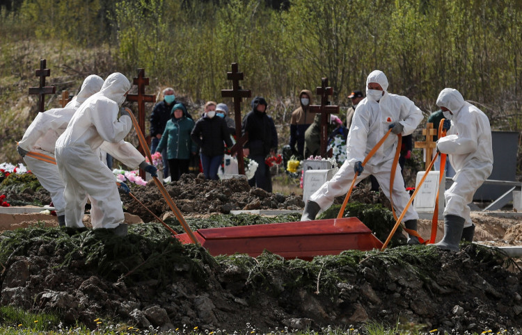 Grave diggers using personal protective equipment (PPE) lower a coffin while burying a person, who presumably died of the coronavirus disease (COVID-19)
